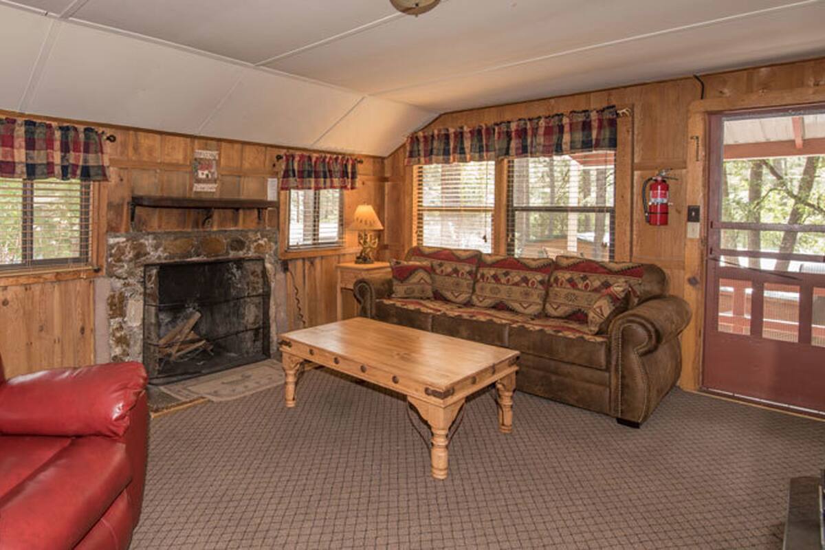 A cozy living room with a fireplace, a red leather chair, a wooden coffee table, and a sofa with patterned cushions.
