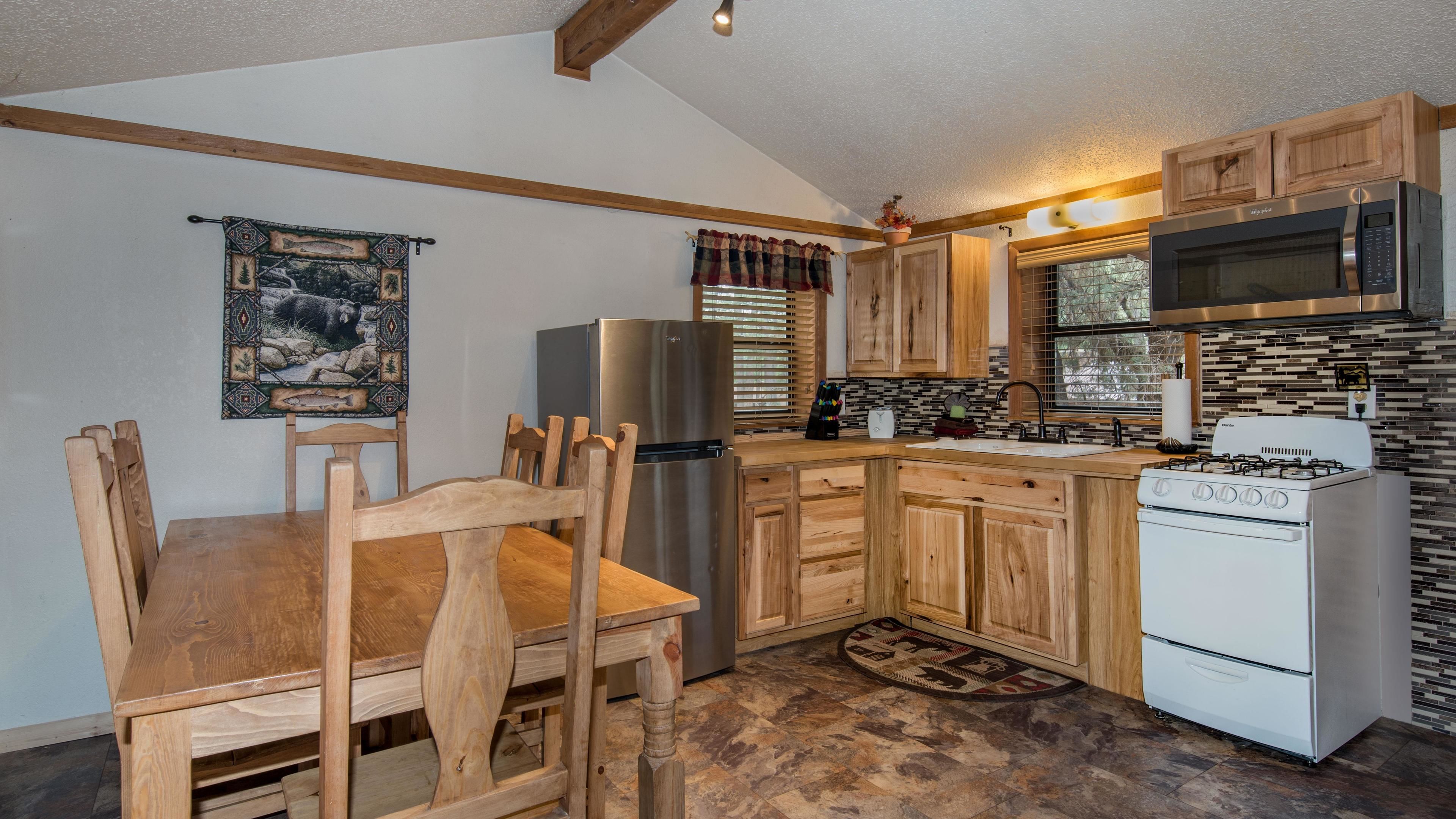 A compact kitchen with wooden cabinets, a stainless steel refrigerator, a microwave, a stove, and a dining table with chairs.