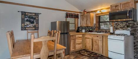 A compact kitchen with wooden cabinets, a stainless steel refrigerator, a microwave, a stove, and a dining table with chairs.