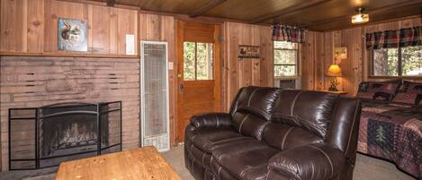A cozy cabin interior with a leather sofa, a fireplace, and a bed with a forest-themed bedspread.