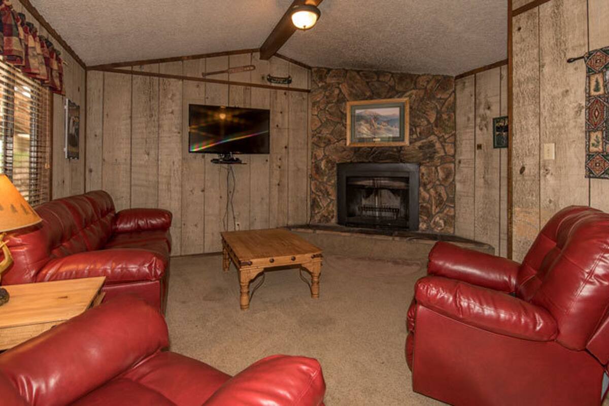 A cozy living room with red leather sofas, a wooden coffee table, a stone fireplace, and a mounted television.