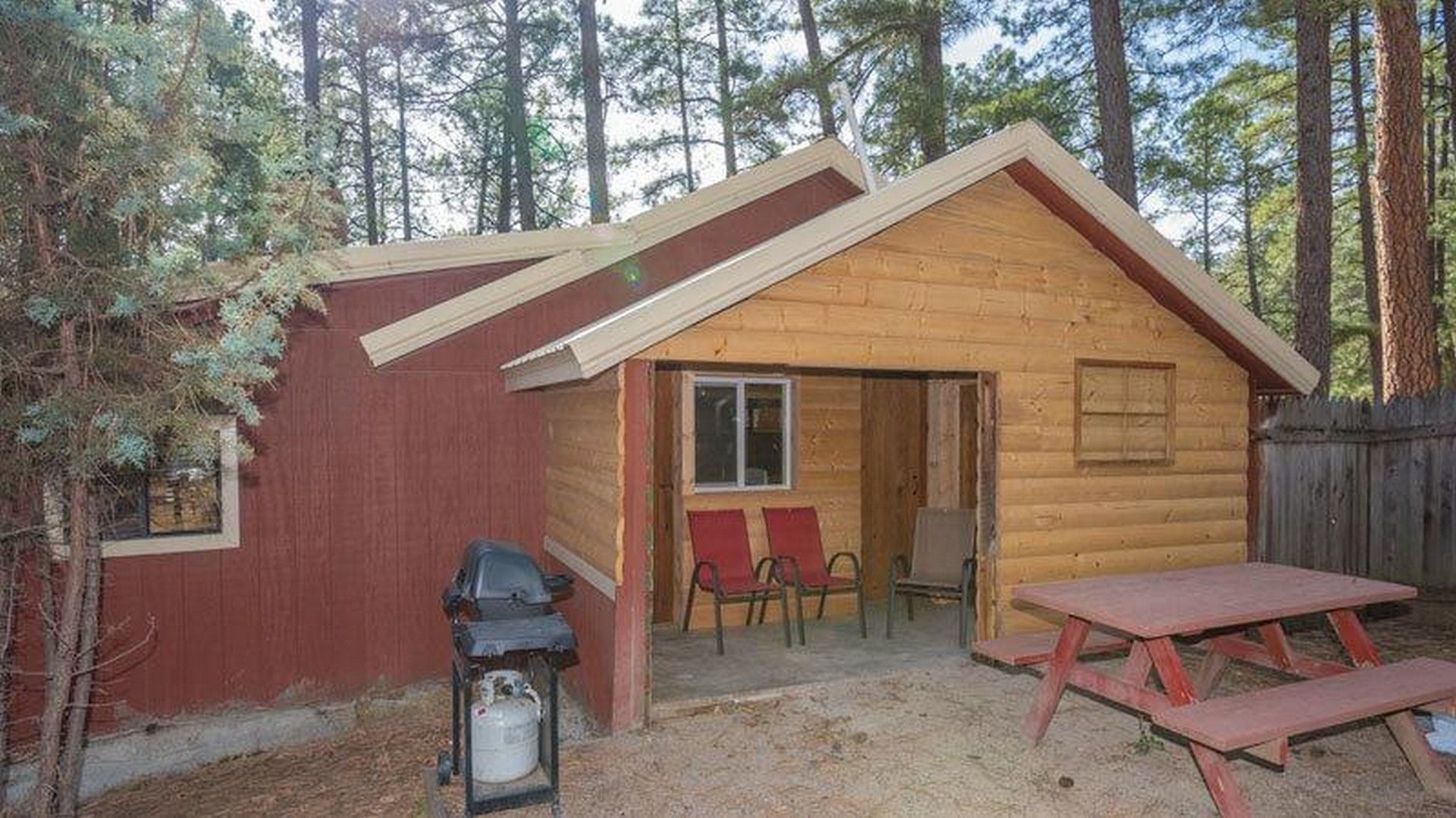 Une petite cabane en bois avec un toit à deux versants, une véranda avec des chaises rouges et une table de pique-nique.