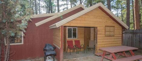 Une petite cabane en bois avec un toit à deux versants, une véranda avec des chaises rouges et une table de pique-nique.
