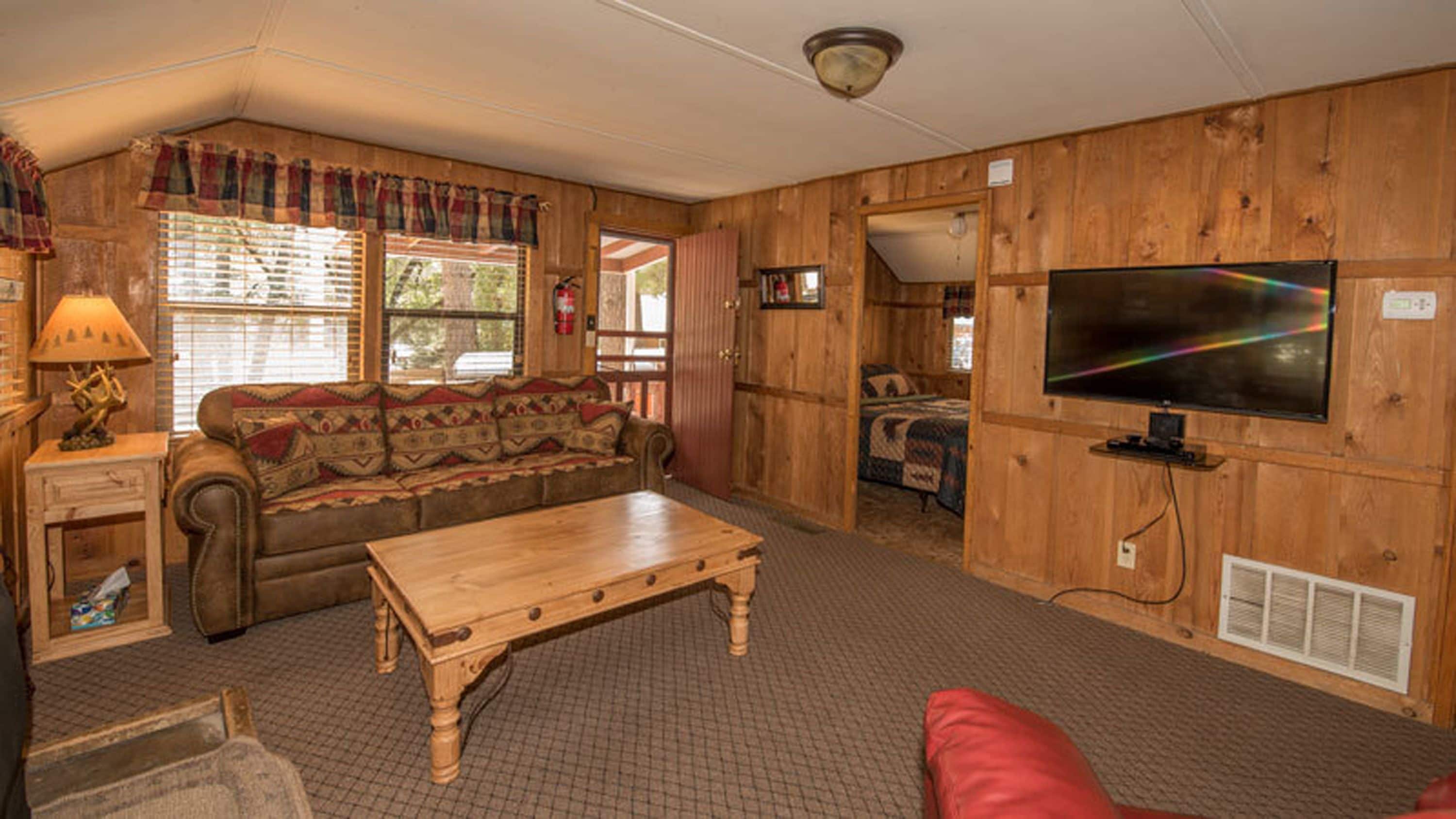 A cozy room with a wooden interior, a sofa, a wooden coffee table, a television, and a window with blinds.