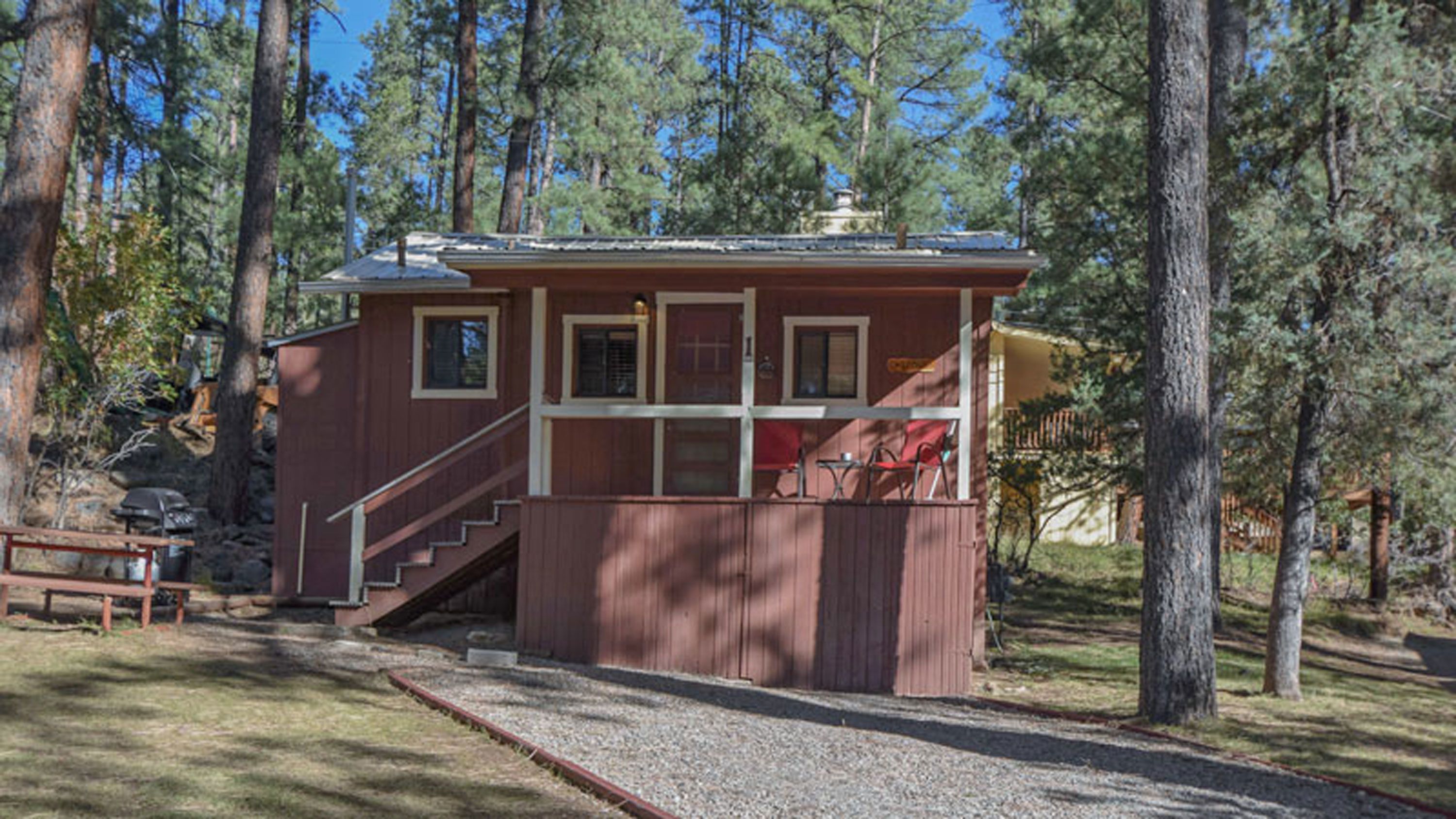 A small cabin with a staircase leading to a deck, surrounded by trees.