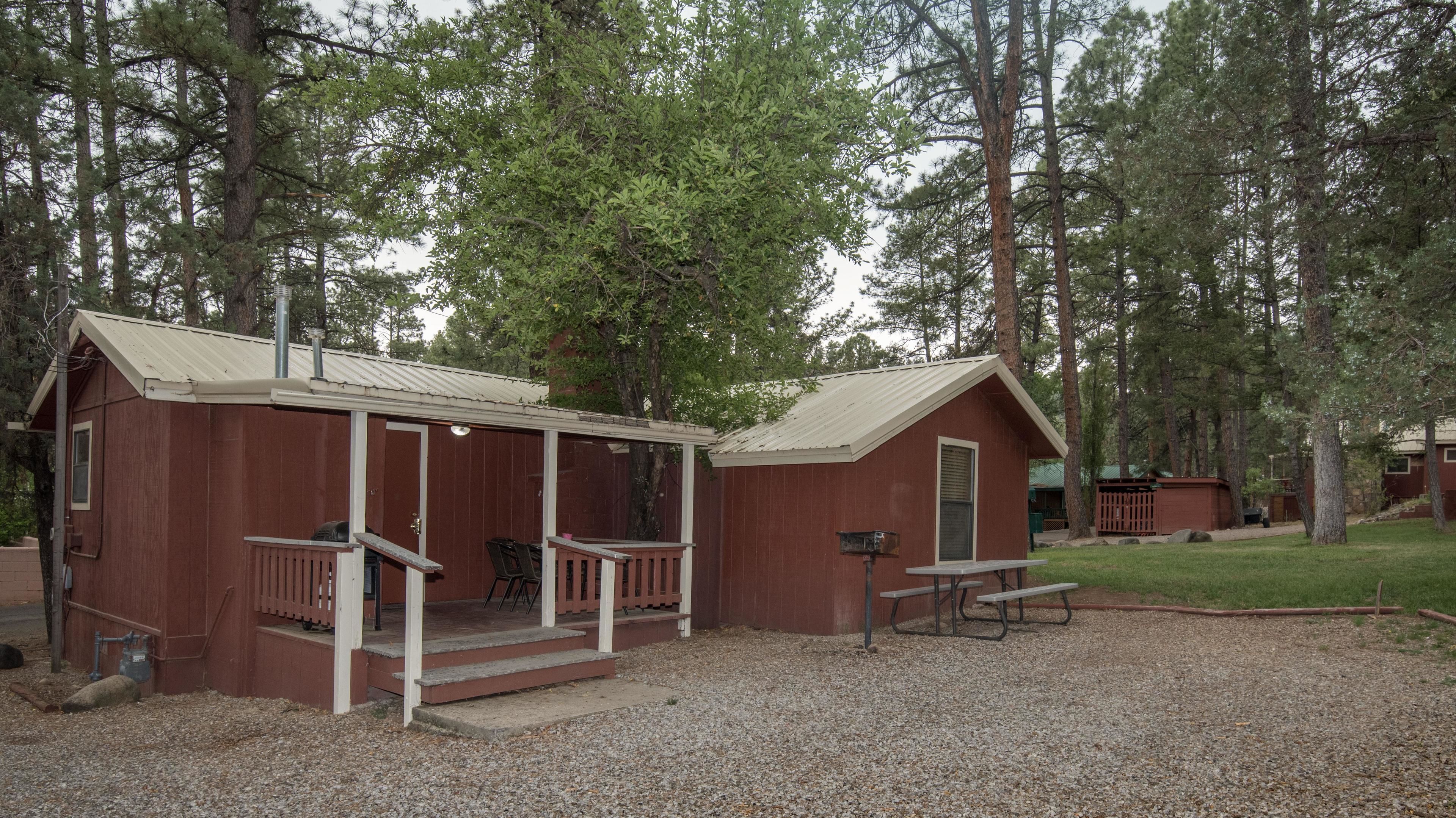 Eine kleine, eingeschossige Holzhütte mit Veranda und Picknicktisch in einem bewaldeten Gebiet.