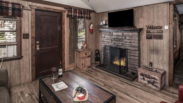 Een gezellige woonkamer met een stenen openhaard, houten wanden en een ruit gordijn.