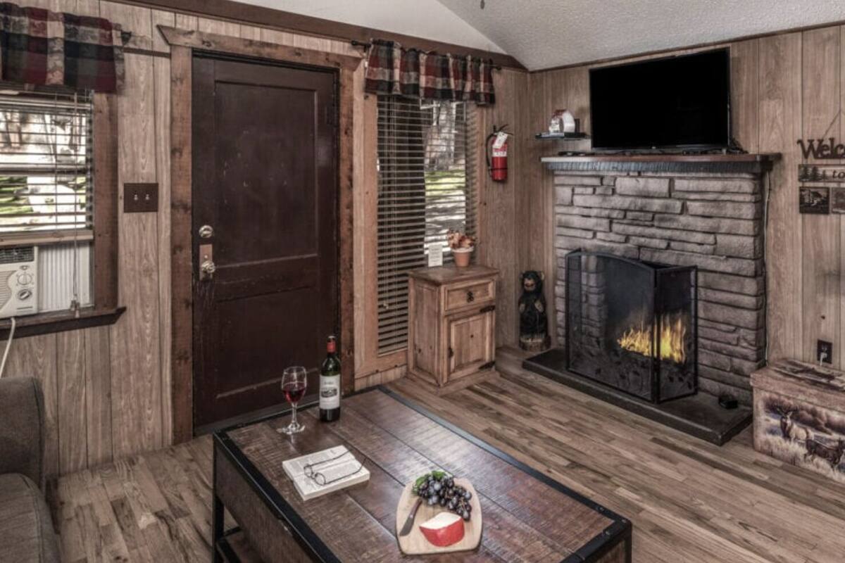 A cozy living room with a stone fireplace, wooden walls, and a plaid curtain.