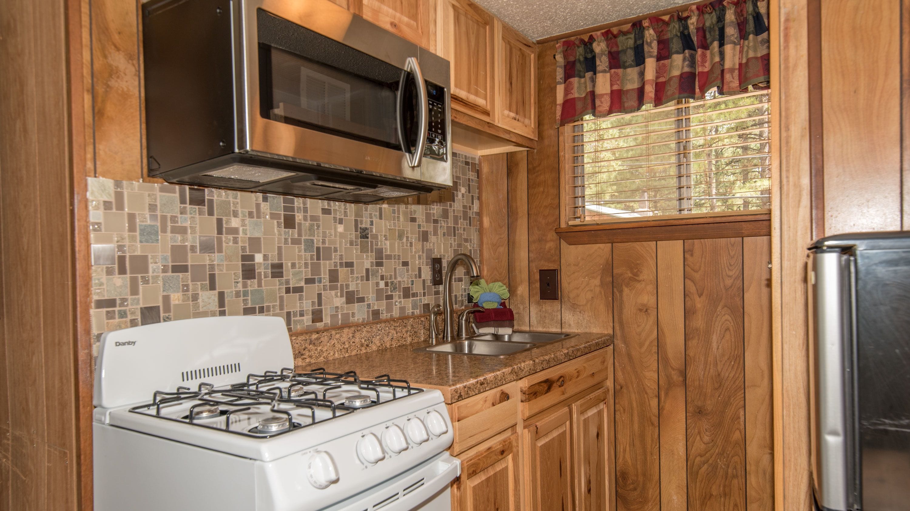 A kitchen with wooden cabinets, a gas stove, a microwave, and a stainless steel refrigerator.