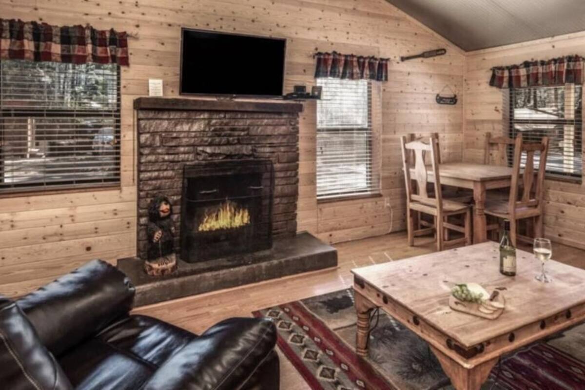 A log cabin interior with a fireplace, leather sofa, dining table, and wooden walls.