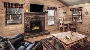 A log cabin interior with a fireplace, leather sofa, dining table, and wooden walls. - Canyon Cabins (Ruidoso)