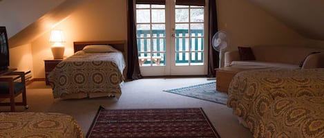 A cozy attic bedroom with two beds, a desk, a chair, a lamp, and a view through a door.