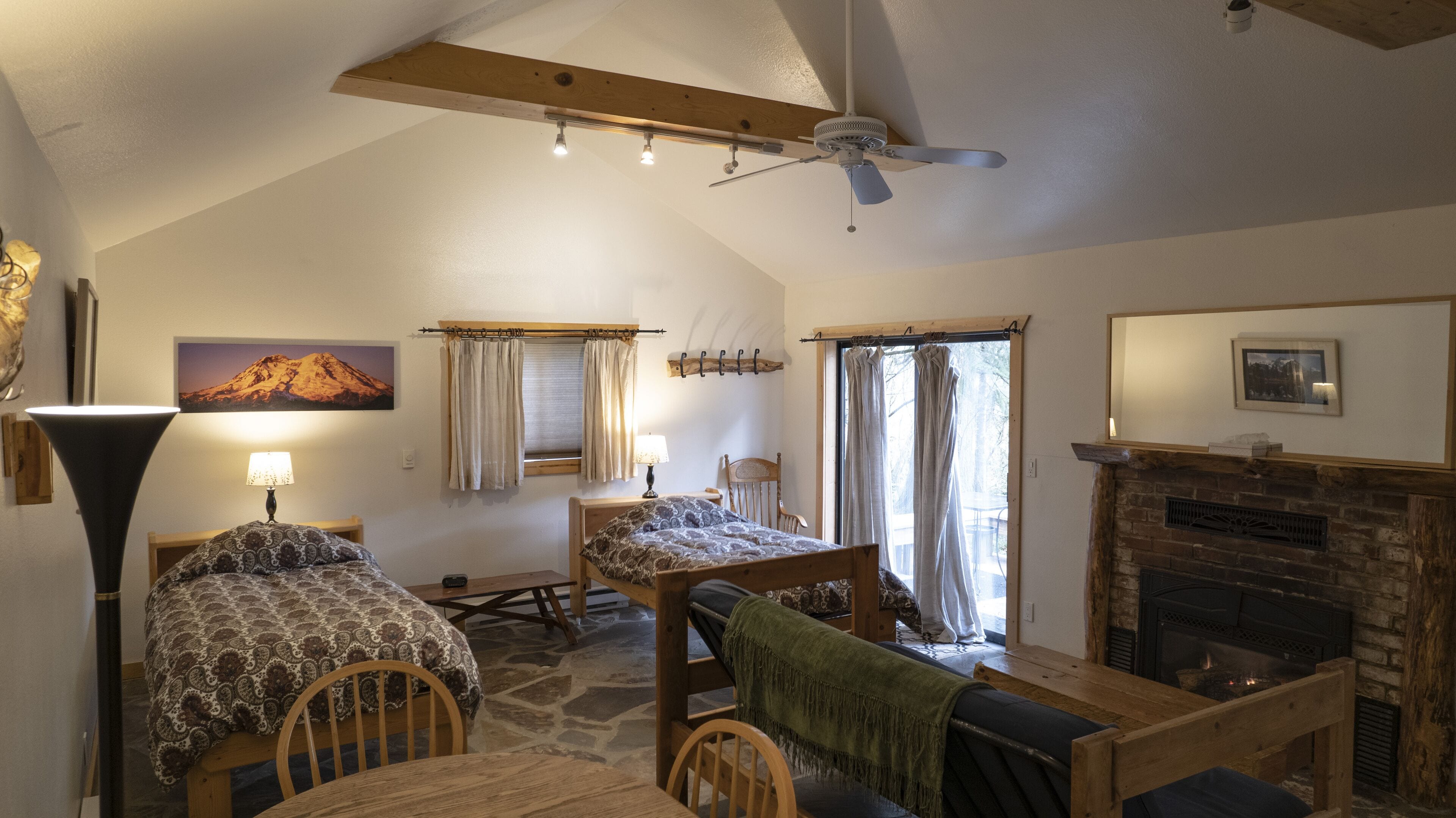 Um quarto de loft acolhedor com teto inclinado, lareira, cama, escrivaninha e mesa de jantar.
