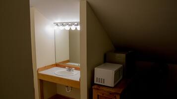 A small, dimly lit bathroom with a wooden vanity, a white sink, and a microwave on a wooden cabinet.