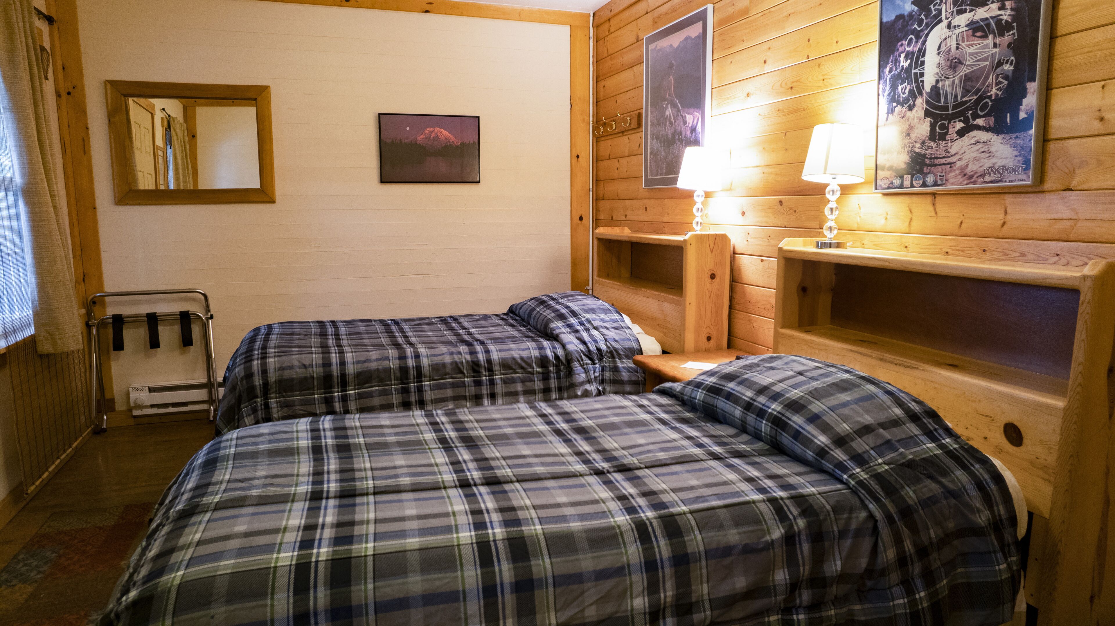 Una habitación con dos camas, cabecero de madera, un espejo, un cuadro enmarco y una lámpara.