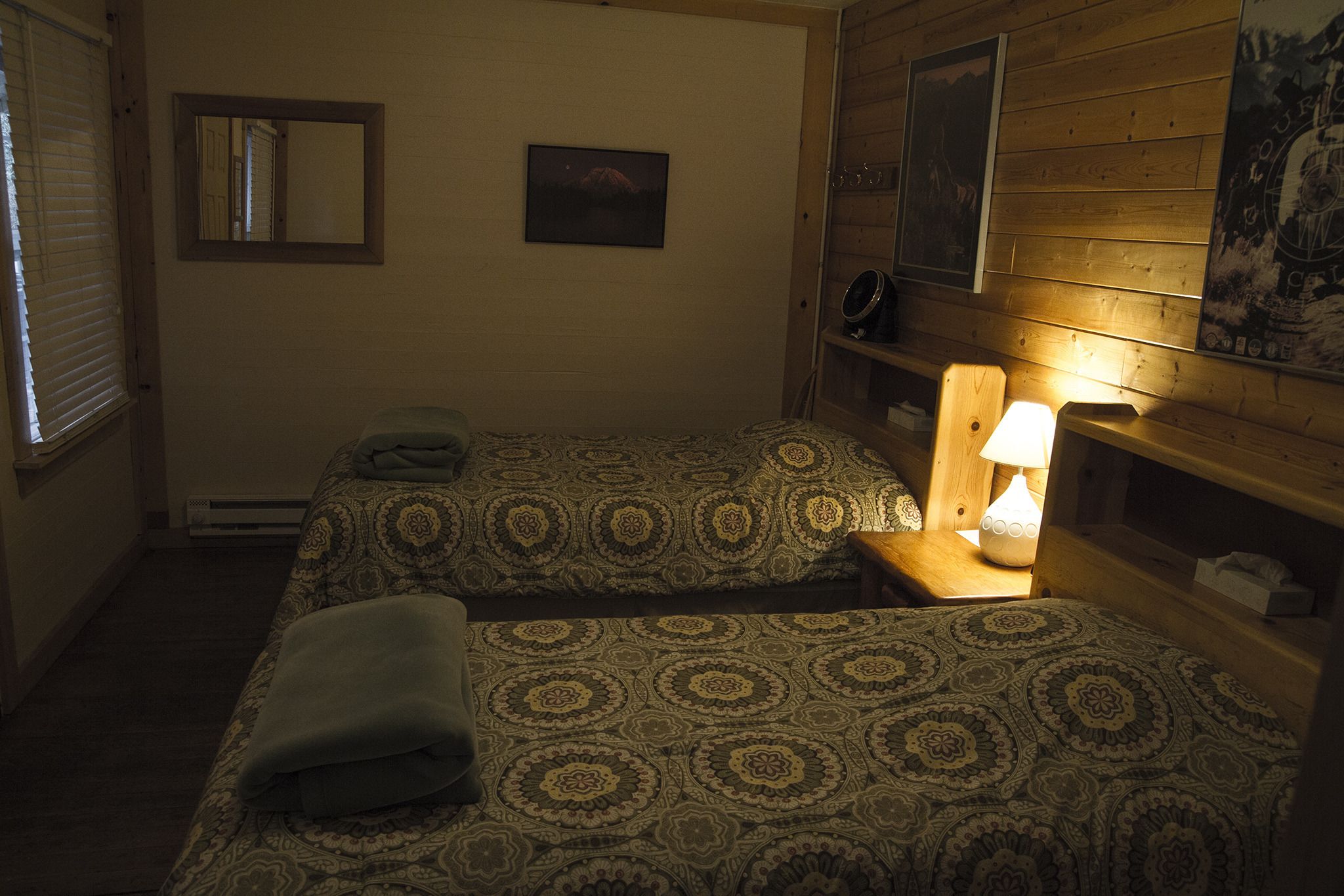 Una habitación pequeña y acogedora con dos camas, un espejo y una estantería con lámpara.