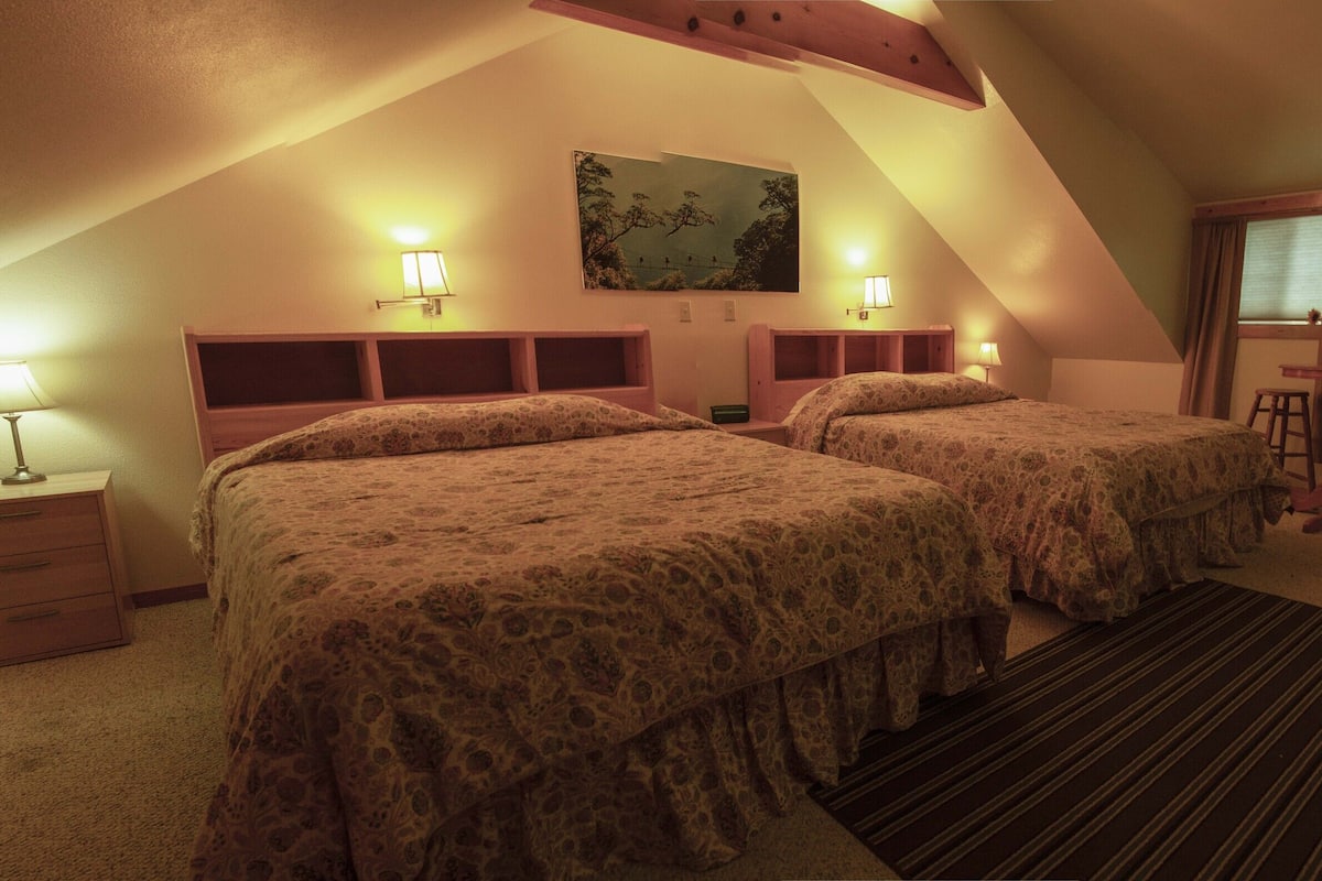 Ein Zimmer mit zwei Betten, einem Schreibtisch, einem Stuhl und einem fensterbelagten Fenster.