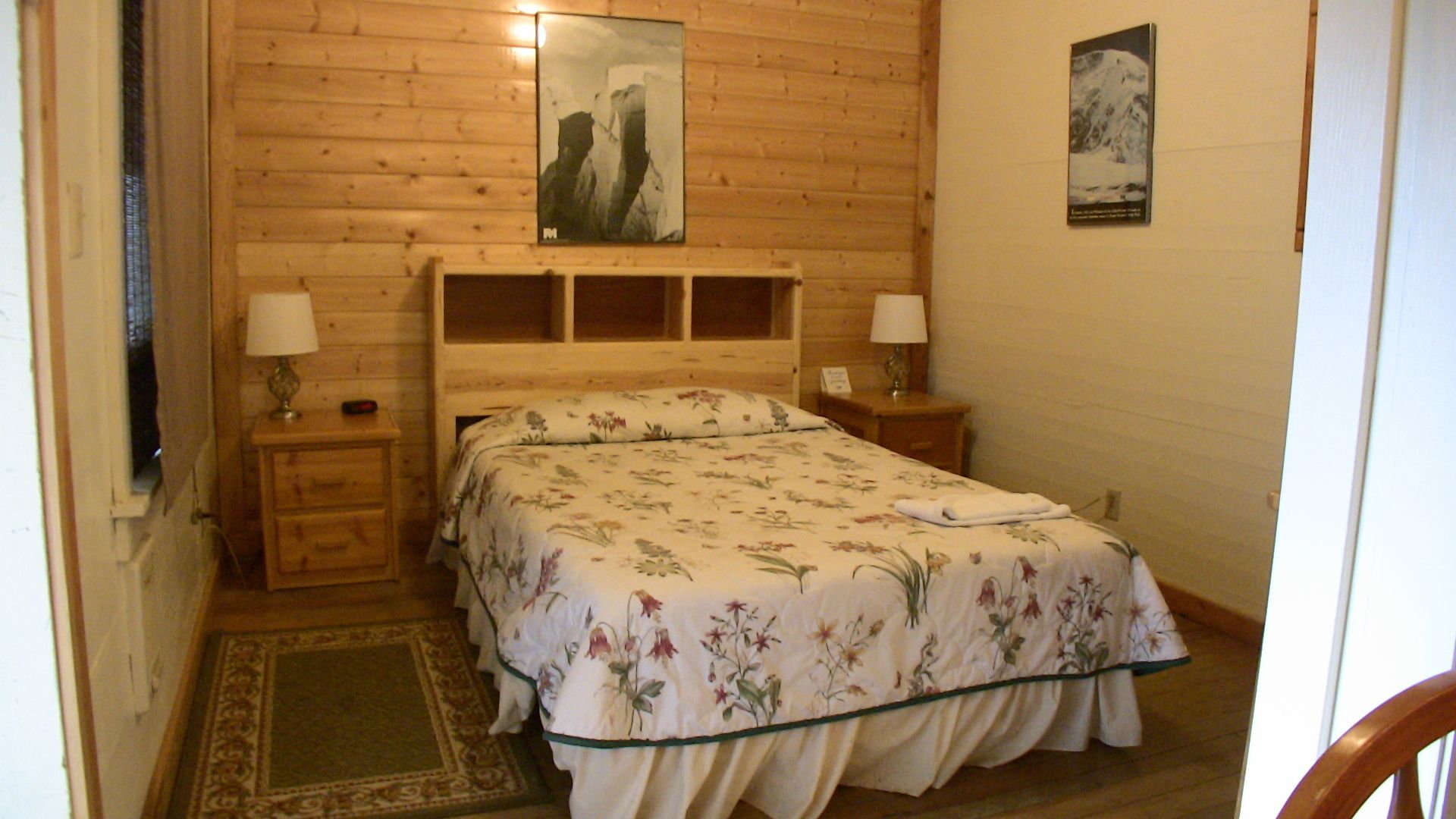 A wooden-paneled bedroom with a bed, two bedside tables, and a nightstand.