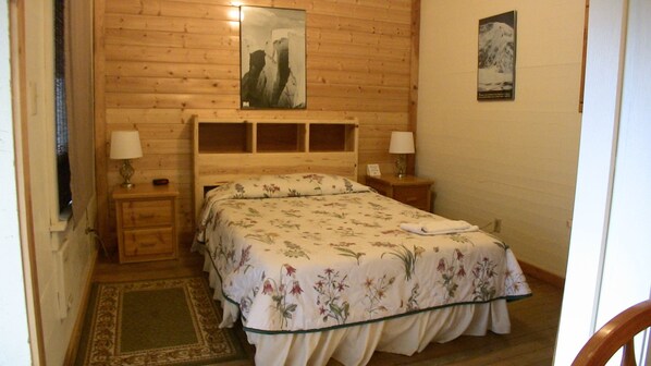 A wooden-paneled bedroom with a bed, two bedside tables, and a nightstand.