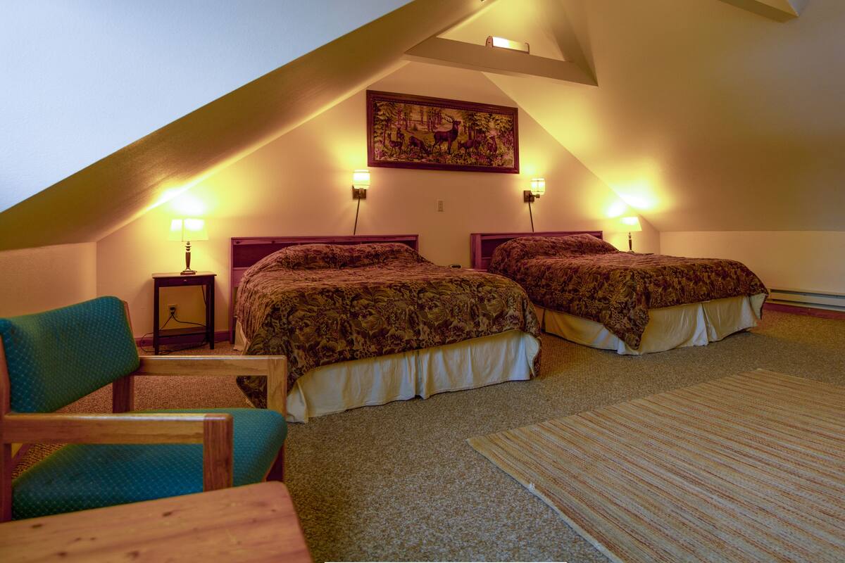 Ein Schlafzimmer mit zwei Betten, einem Sessel, einem Tisch und einem Bild an der Wand.