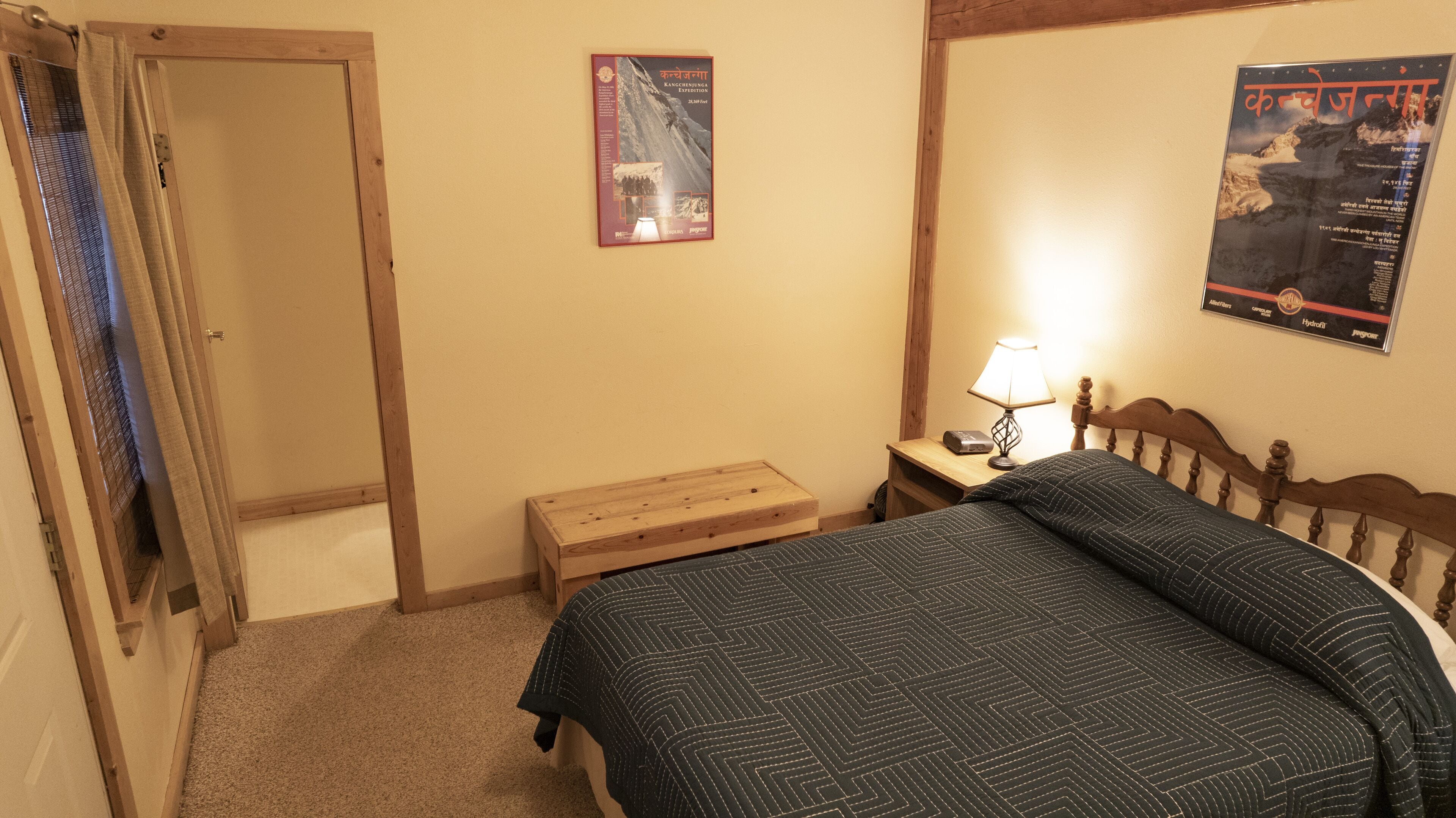 A bedroom with a bed, a nightstand, a lamp, a poster on the wall, and a door.