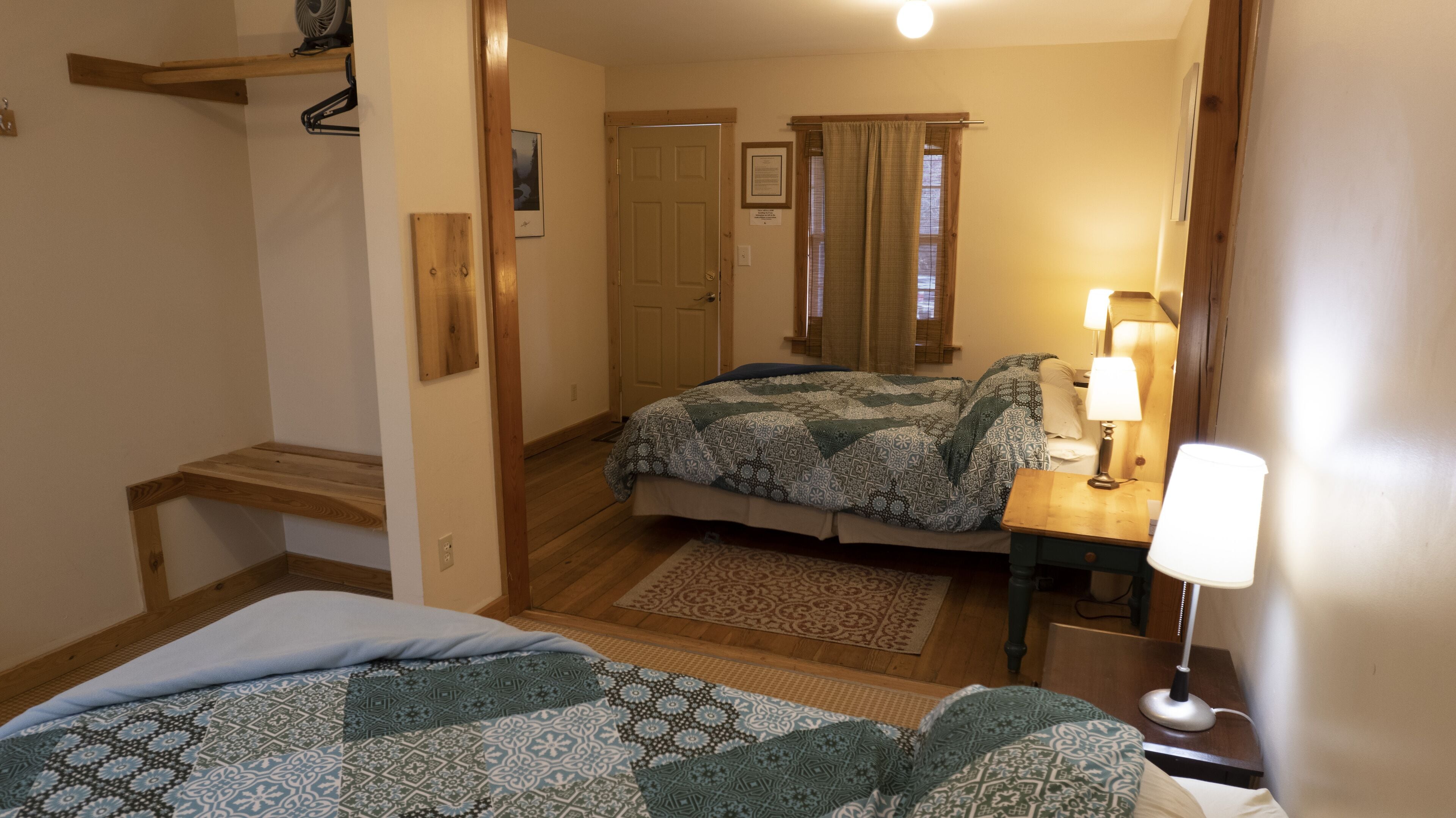 A bedroom with a bed, a nightstand with a lamp, a wooden bench, and a door leading to another room.