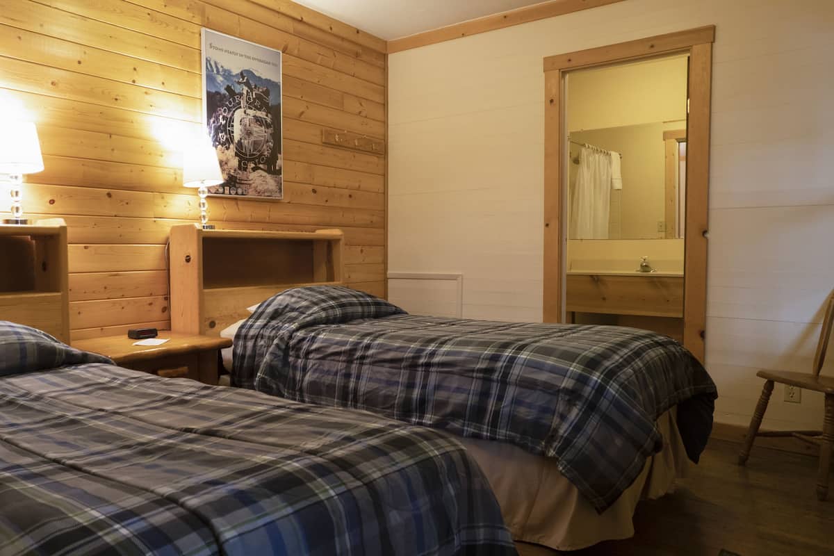 Ein Zimmer mit zwei Betten, Holzkopfteilen, einer Holzwand, einem Poster, einem Spiegel und einem Stuhl.