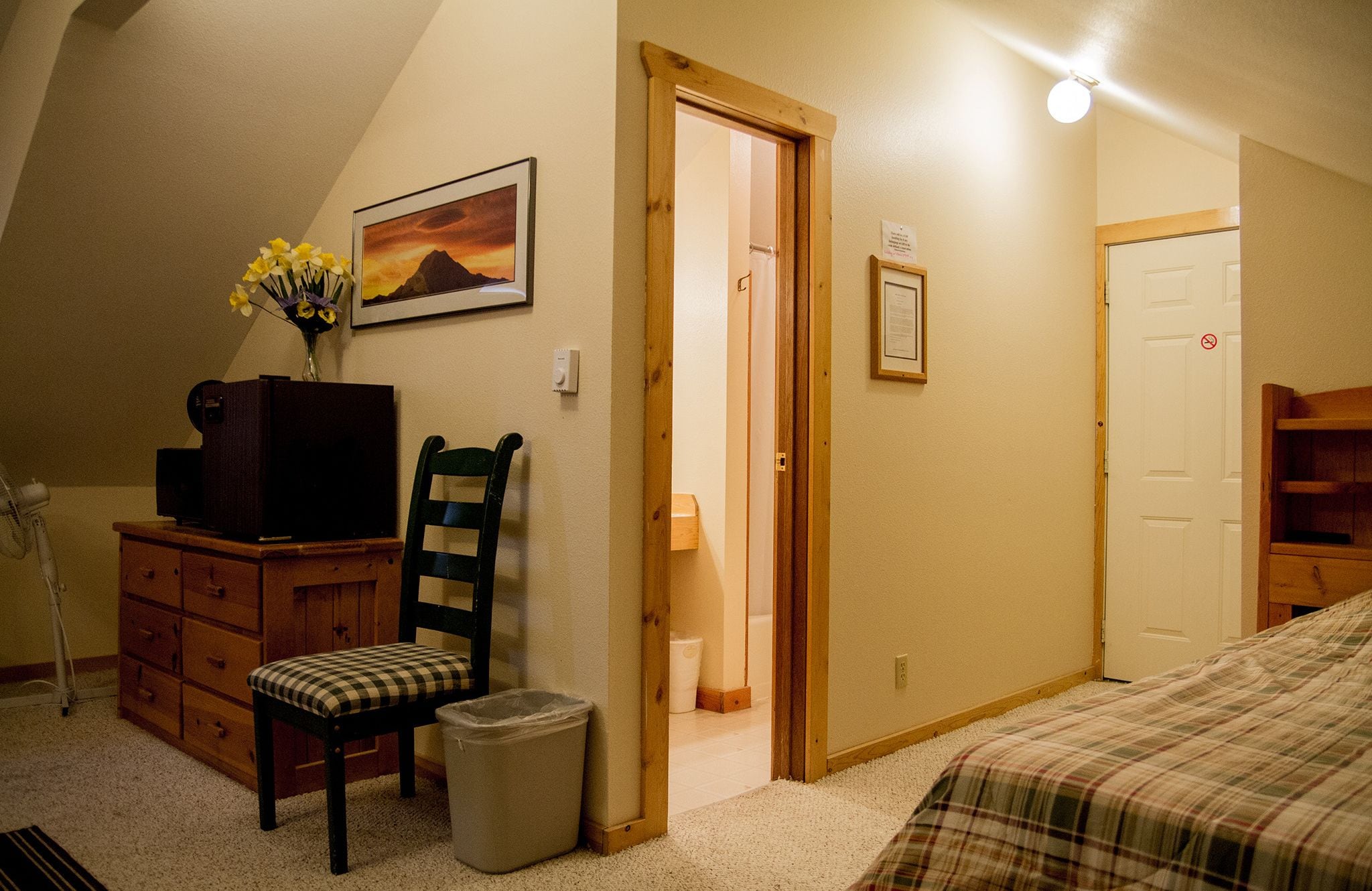Une chambre à coucher avec un lit, une chaise, une commode, un téléviseur et un tableau accroché au mur.