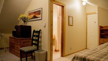 Une chambre à coucher avec un lit, une chaise, une commode, un téléviseur et un tableau accroché au mur.