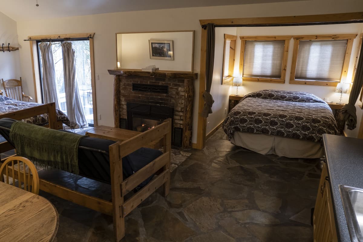 Ein gemütliches Zimmer mit Steinfußboden, Kamin, einem Bett, einem Holztisch und einem Stuhl.