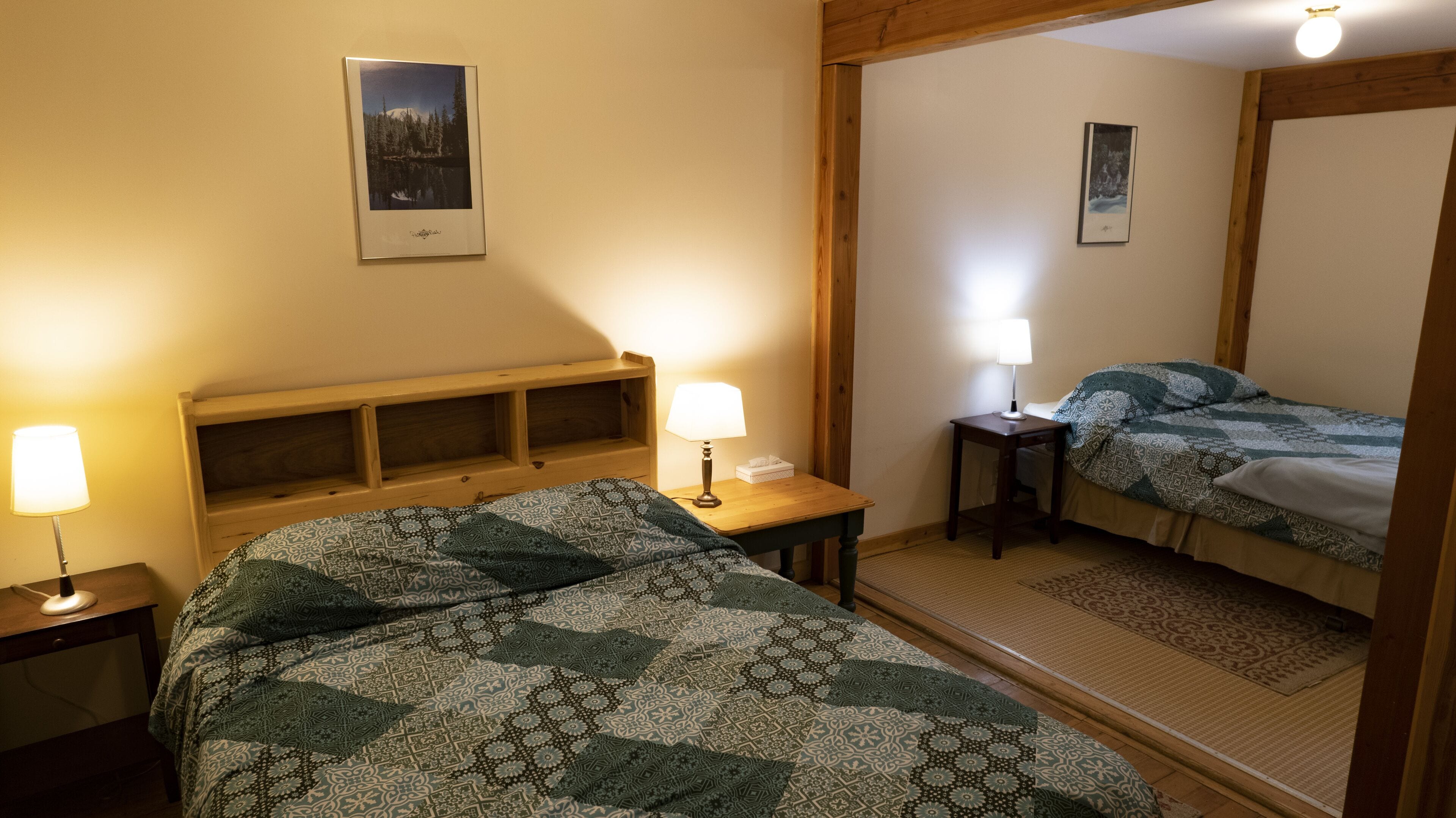 A hotel room with a bed, bedside table, lamp, and a mirror reflecting the bed.