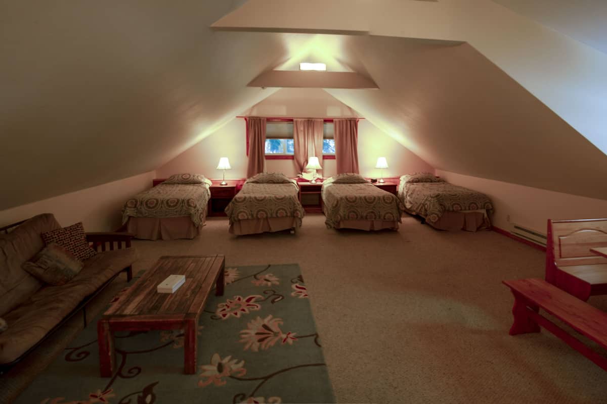 Ein gemütliches Schlafzimmer im Dachgeschoss mit vier Einzelbetten, einer Holzbank, einem kleinen Tisch und einem Fenster mit Vorhängen.