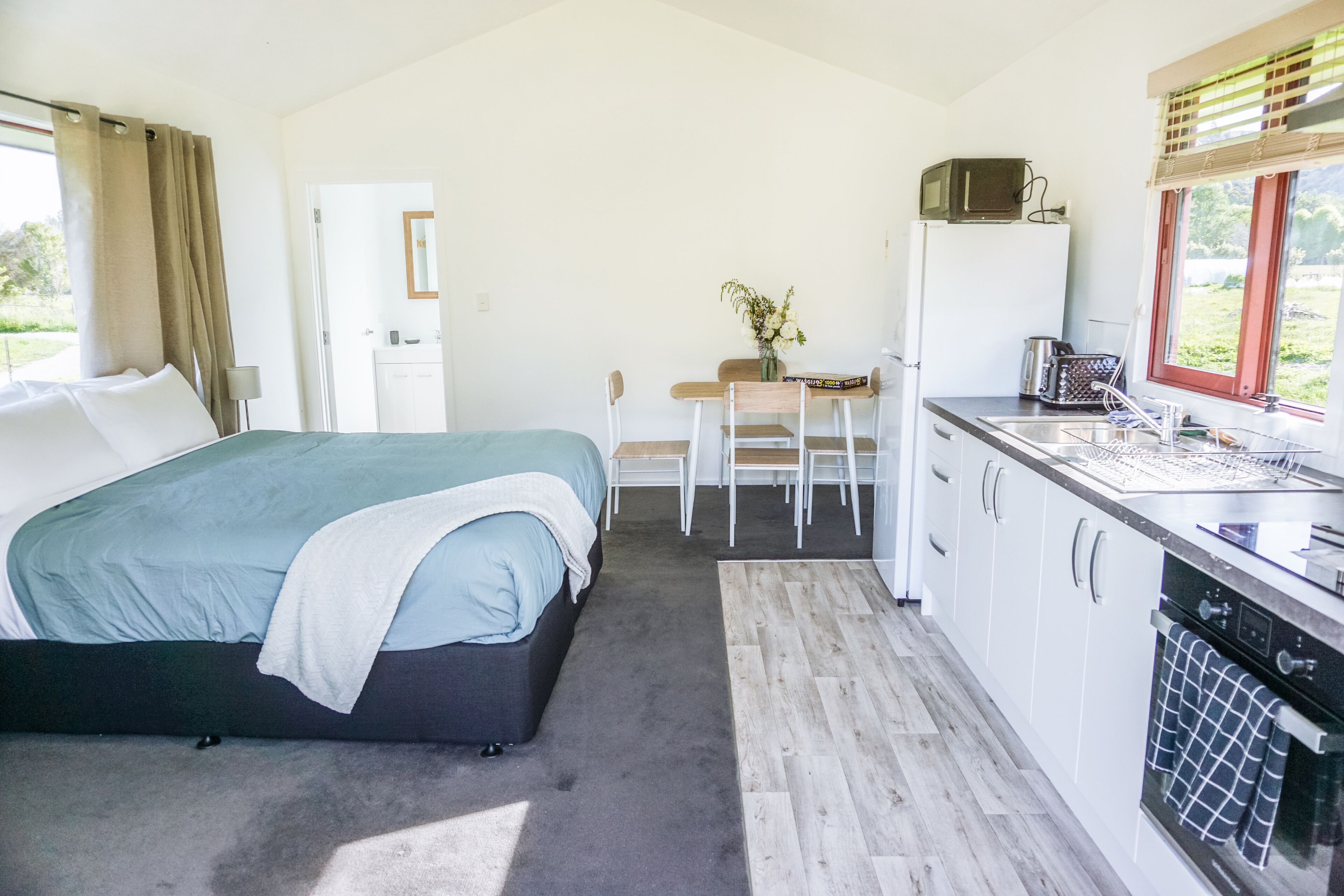 A bedroom with a bed, a small desk, a chair, and a kitchenette with a refrigerator, microwave, and sink.