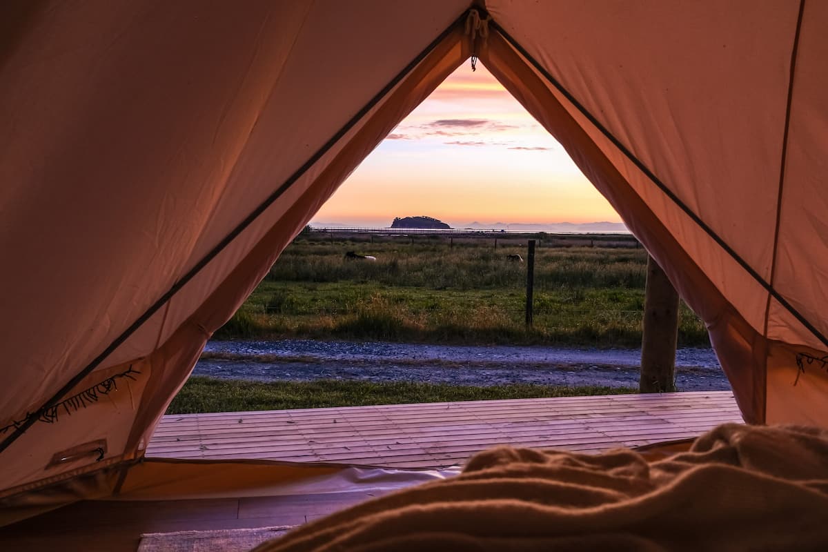 A tent with a view of a grassy field and a distant island at sunset.