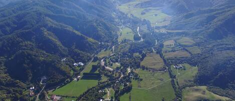 Une vue aérienne d’une vallée avec des champs verdoyants, des maisons dispersées et une route sinueuse.