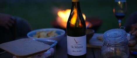 A bottle of Te Manoa wine, a wooden cutting board with food, a glass jar, and a bowl of chips on a table.