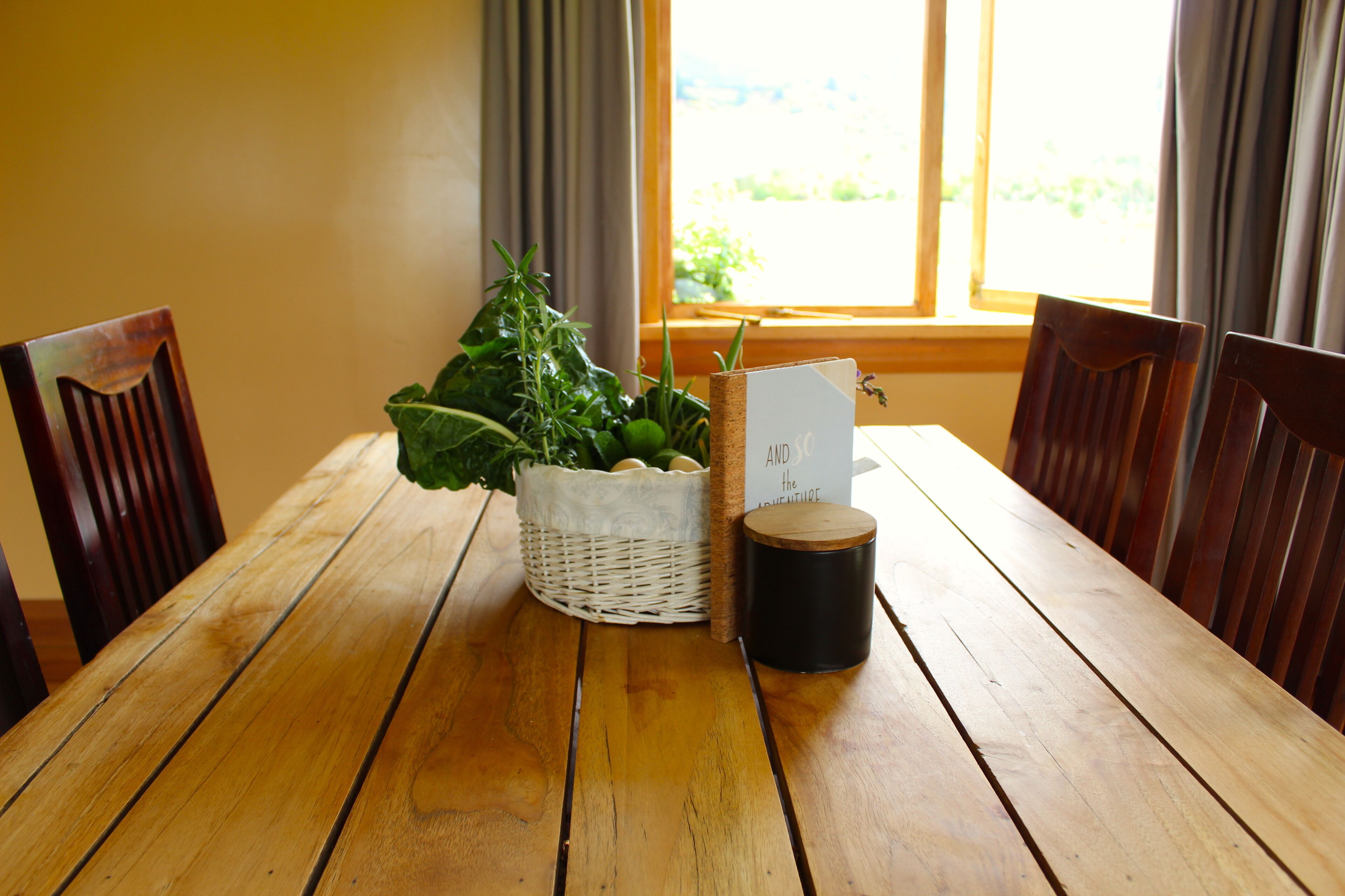 Ein Holzespeisetisch mit Stühlen, ein gewebter Korb mit Pflanzen, eine schwarze Kerze und eine Karte.