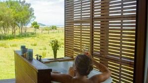 A bathtub with a view of a grassy field and trees. - The Barn Cabins & Camp (Marahau)