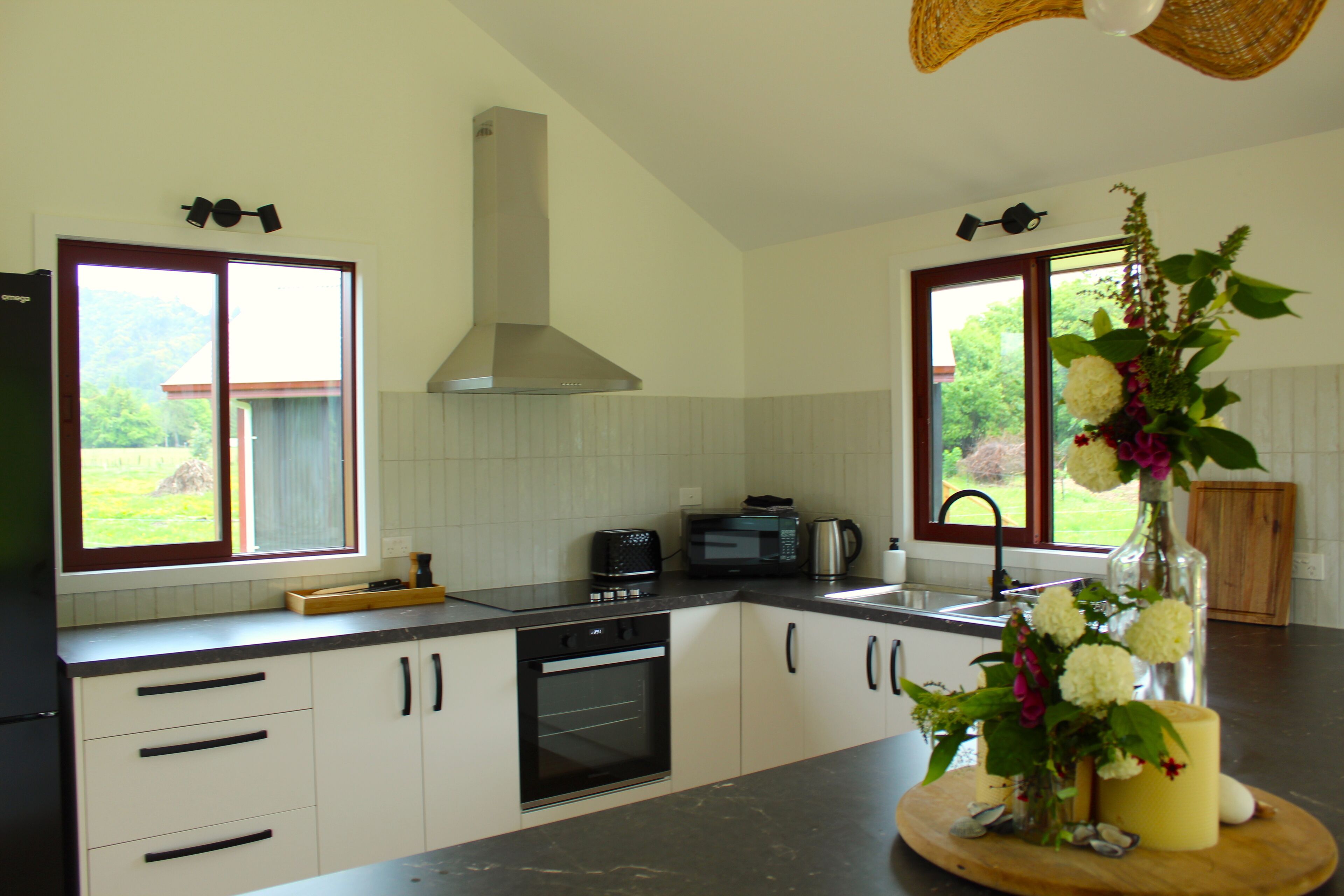 A modern kitchen with white cabinets, a built-in oven, a microwave, and a large window with a view of greenery.