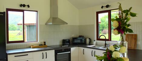 A modern kitchen with white cabinets, a built-in oven, a microwave, and a large window with a view of greenery.