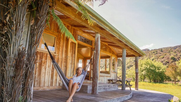 A wooden cabin with a porch, a hammock, and a picnic table. - The Barn Cabins & Camp (Marahau)