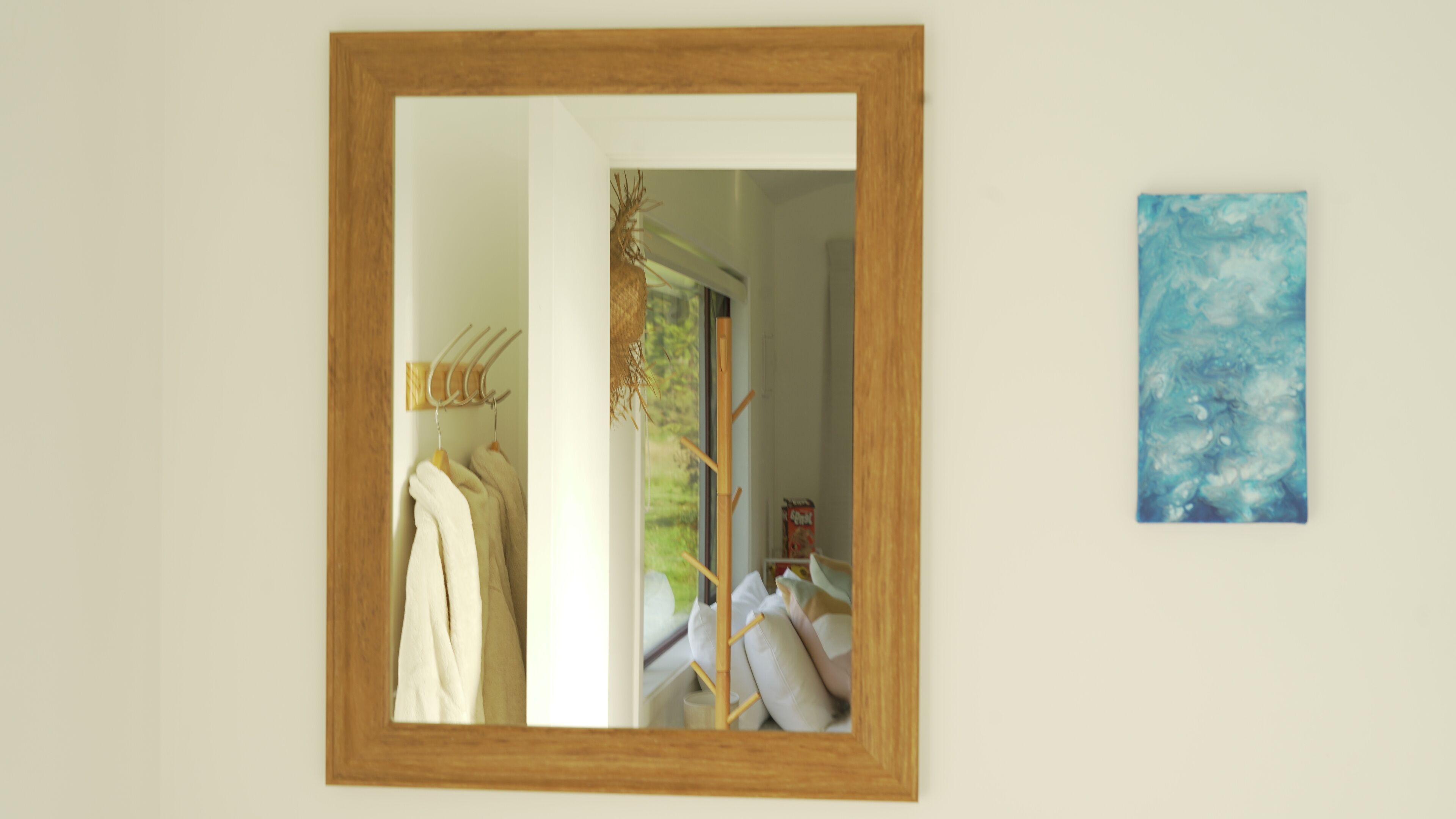 Un miroir avec un cadre en bois, un porte-serviettes avec des serviettes, un tableau et une fenêtre donnant sur un paysage verdoyant.