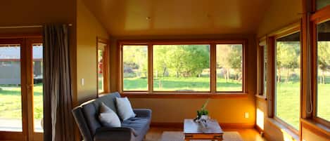 A spacious living room with a sofa, a coffee table, and large windows offering a view of a green landscape.