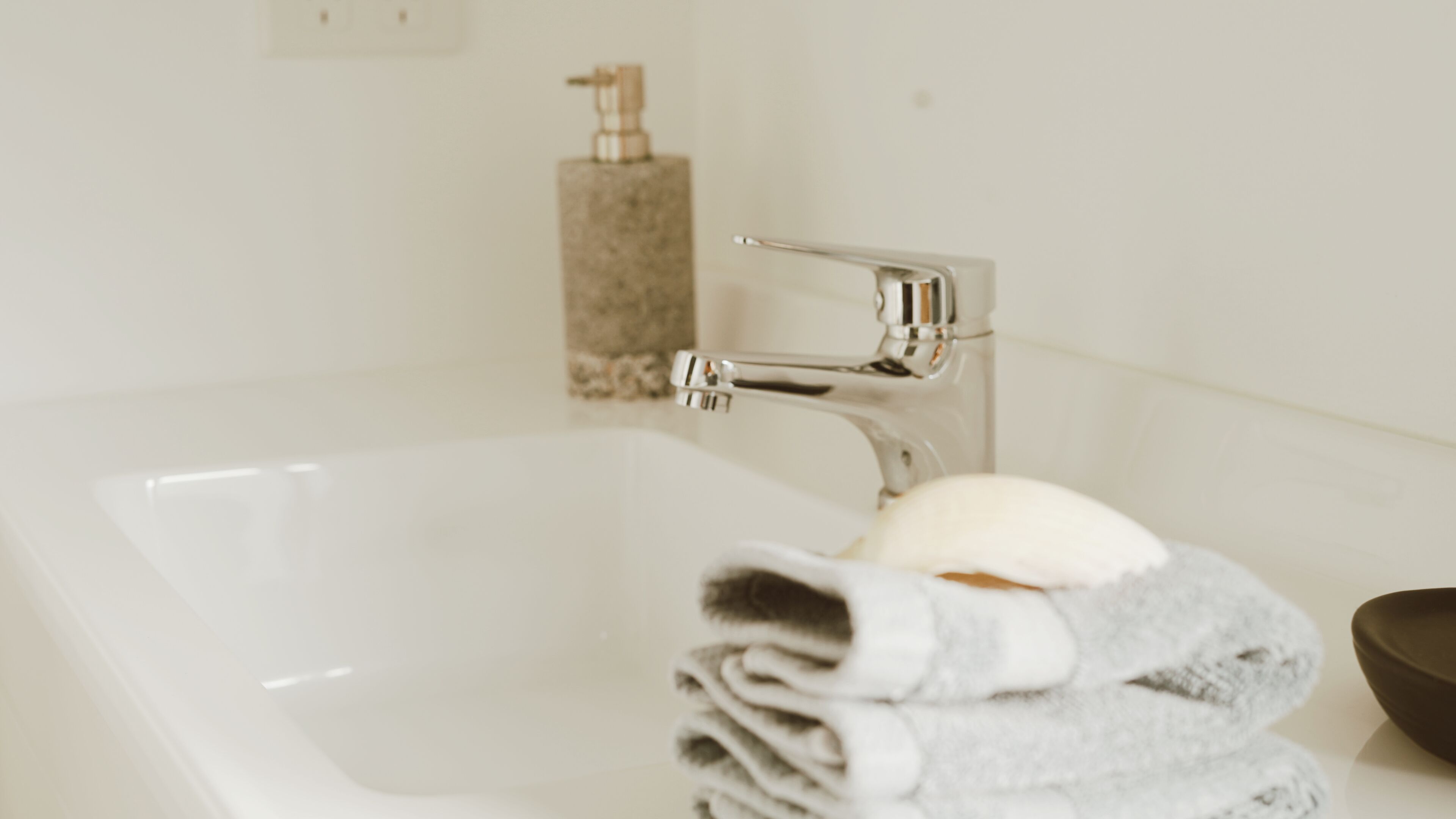 Un baño con lavamanos blanco, grifo cromado, dispensador de jabón y toallero con toallas dobladas.