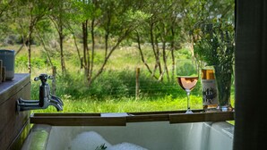 A bathtub with a glass of wine and a bottle, surrounded by greenery. - The Barn Cabins & Camp (Marahau)