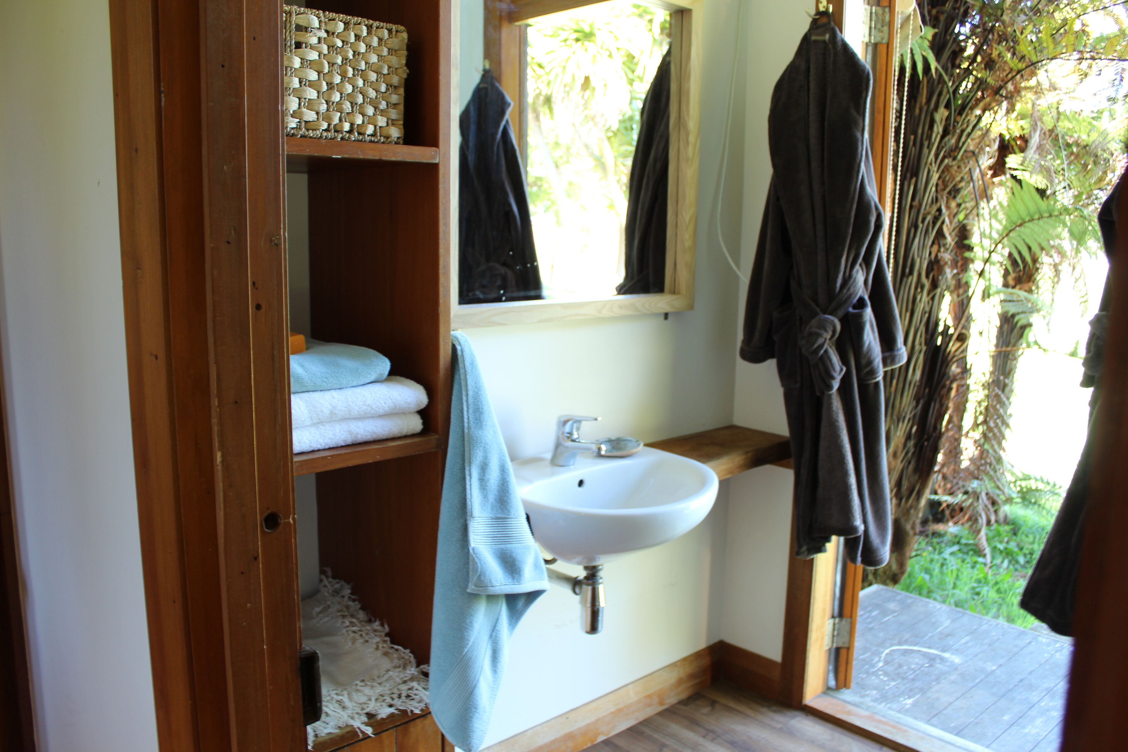 Un baño con estante de madera, lavamanos y ventana.