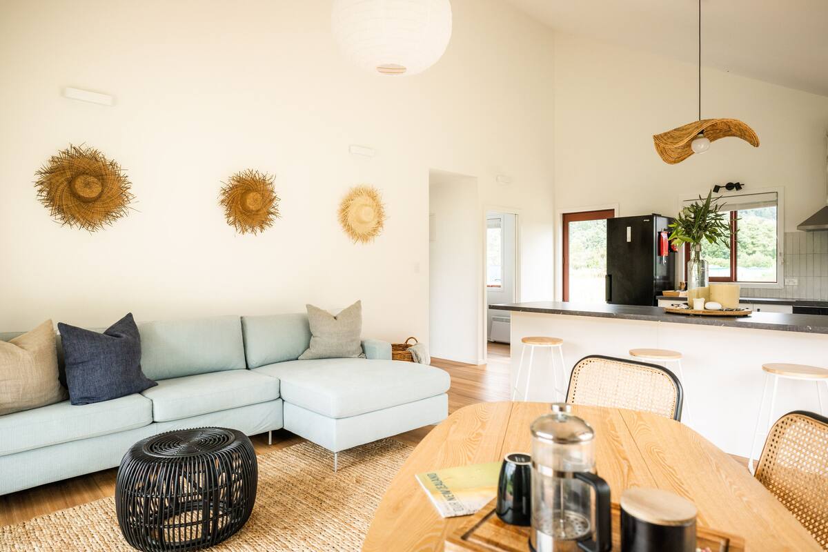 A modern living room with a light blue sofa, a wooden dining table, and a kitchen in the background.