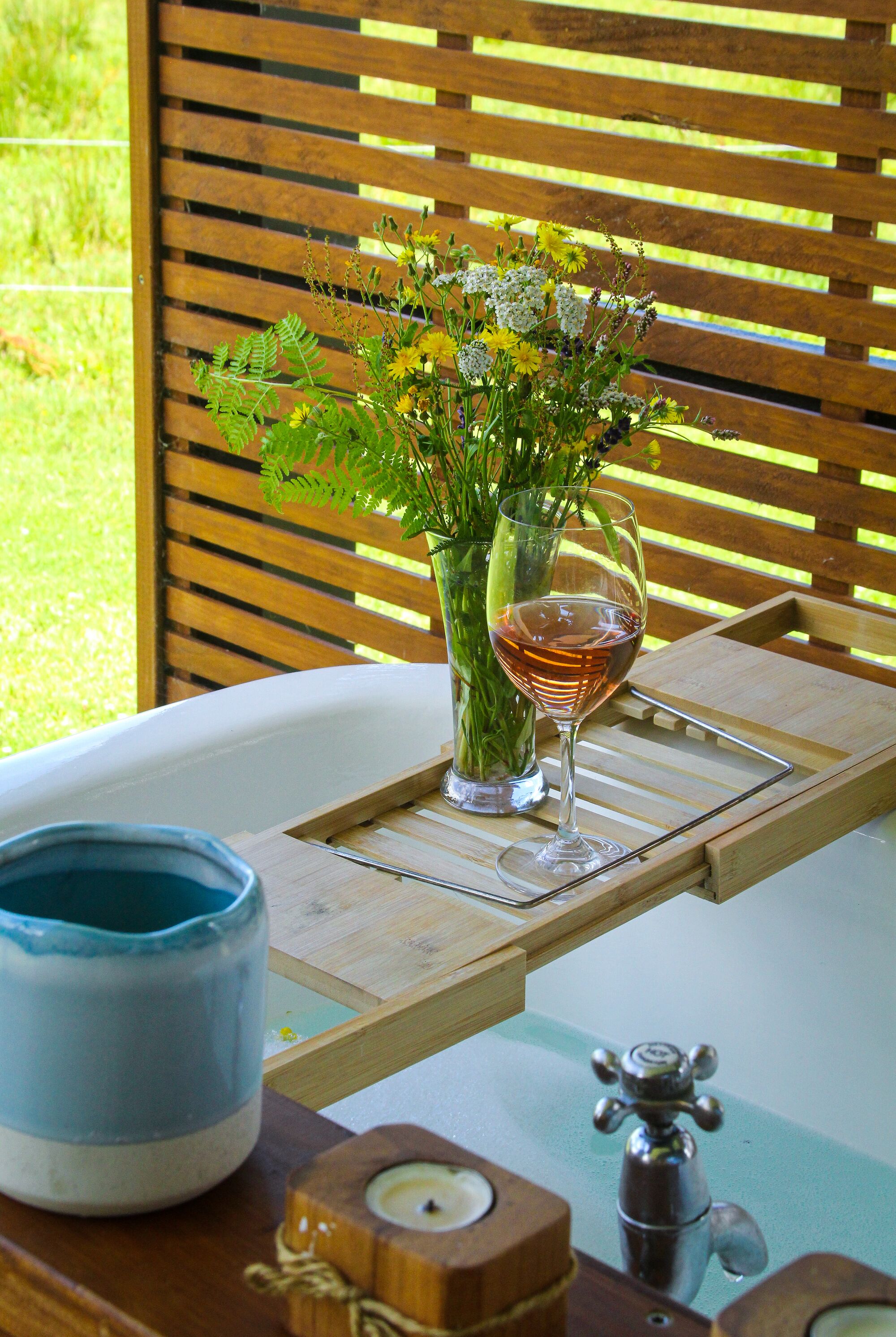 Un banco de madera con una copa de vino tinto y un jarrón de flores.