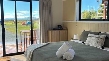 A modern bedroom with a large bed, a view of a grassy area with picnic tables, and a wooden ceiling.