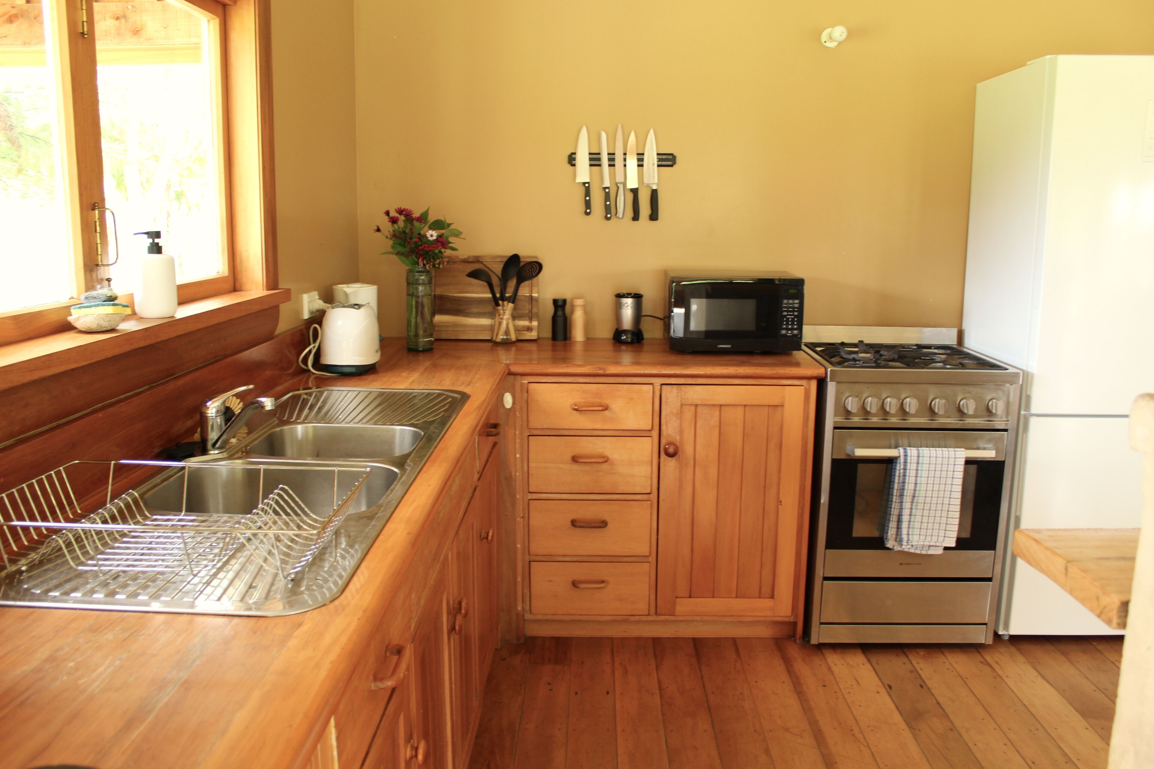 Una cocina con armarios de madera, un lavamanos de acero inoxidable, un microondas y un horno.